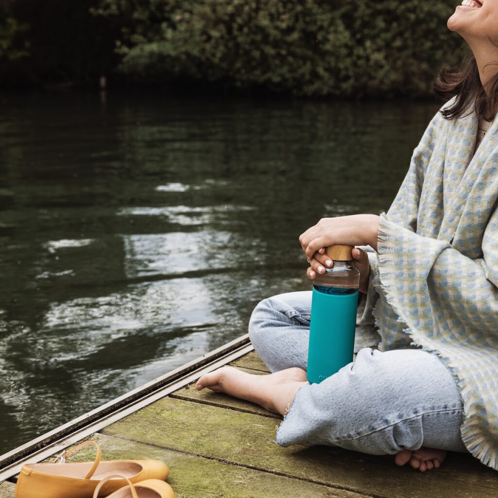 woman in gray sweater and gray pants sitting on brown wooden boat on river during daytime